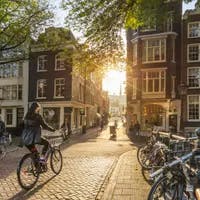 Amsterdam, Netherlands - September 22, 2021: Early morning in Amsterdam. Artistic image.  People ride bicycles, the ancient European city of Amsterdam. Sunlight and silhouettes, beautiful downtown houses.  Amsterdam, Holland, Netherlands, Europe