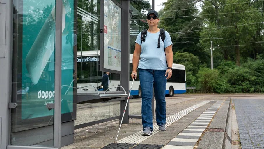 A person with a visual disability walks to the bus stop.