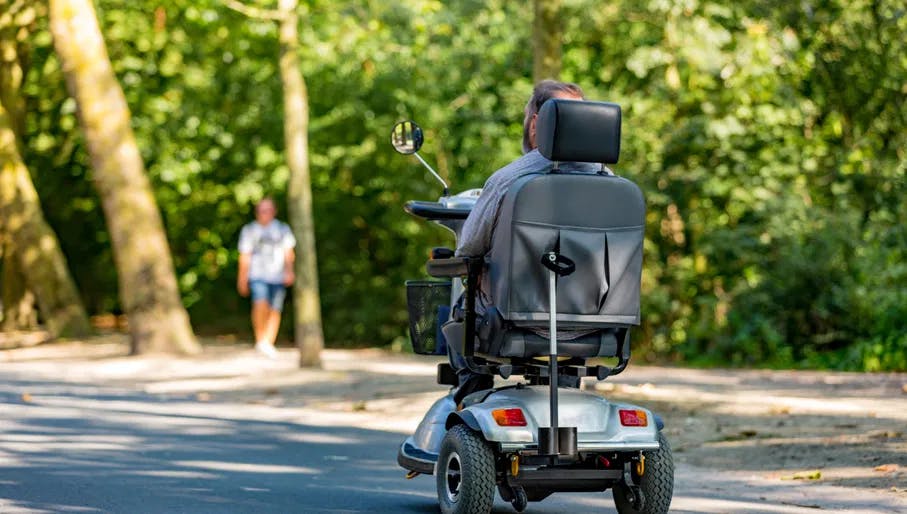 A older man riding in an electric wheelchair in a sunny and green Amsterdam Vondelpark in the Netherlands.