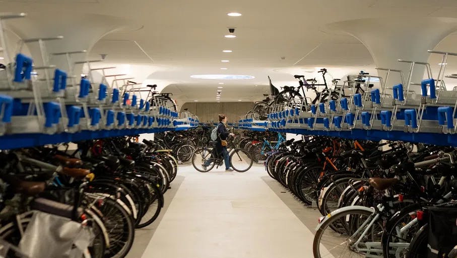 Woman walking through the underground bike parking with a bike in her hand. On de sides bicycle storages