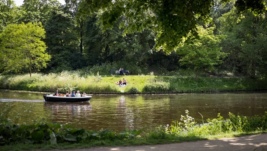People on a boat passing by over the water in De Bolwerken, a city park in the center of Haarlem.