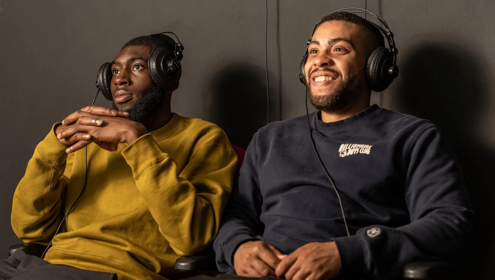 Two men wearing headphones and watching a video that is part of an exhibition at CBK Zuidoost.