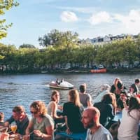 Waterkant people sitting on the terrace next to the water and a water bike passing by