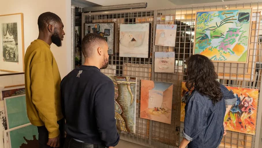 Two men visit the art loan of CBK Zuidoost and are listening to the story of the museum employee.