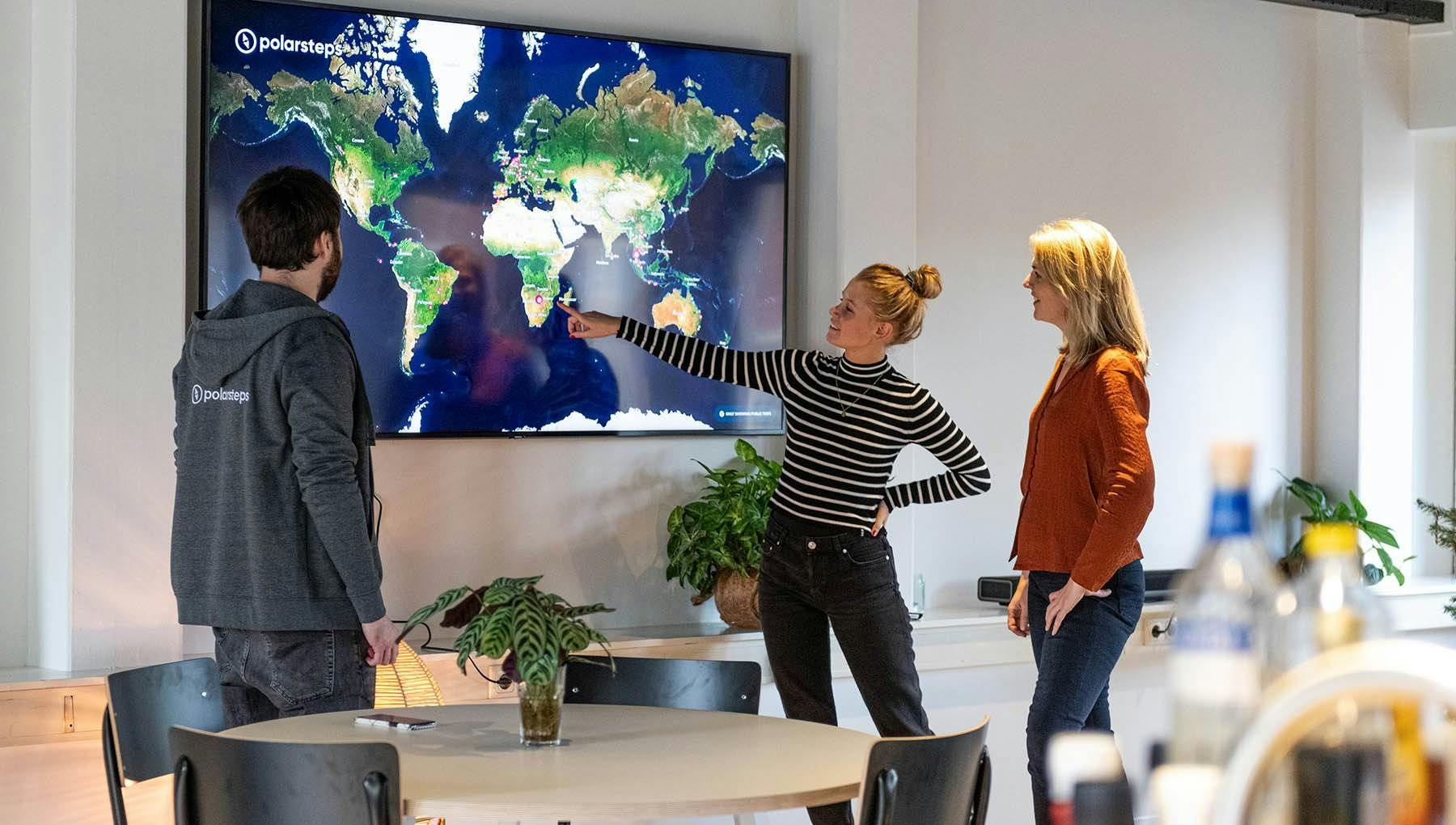 Polarsteps employees in their office pointing at a screen showing a world map.