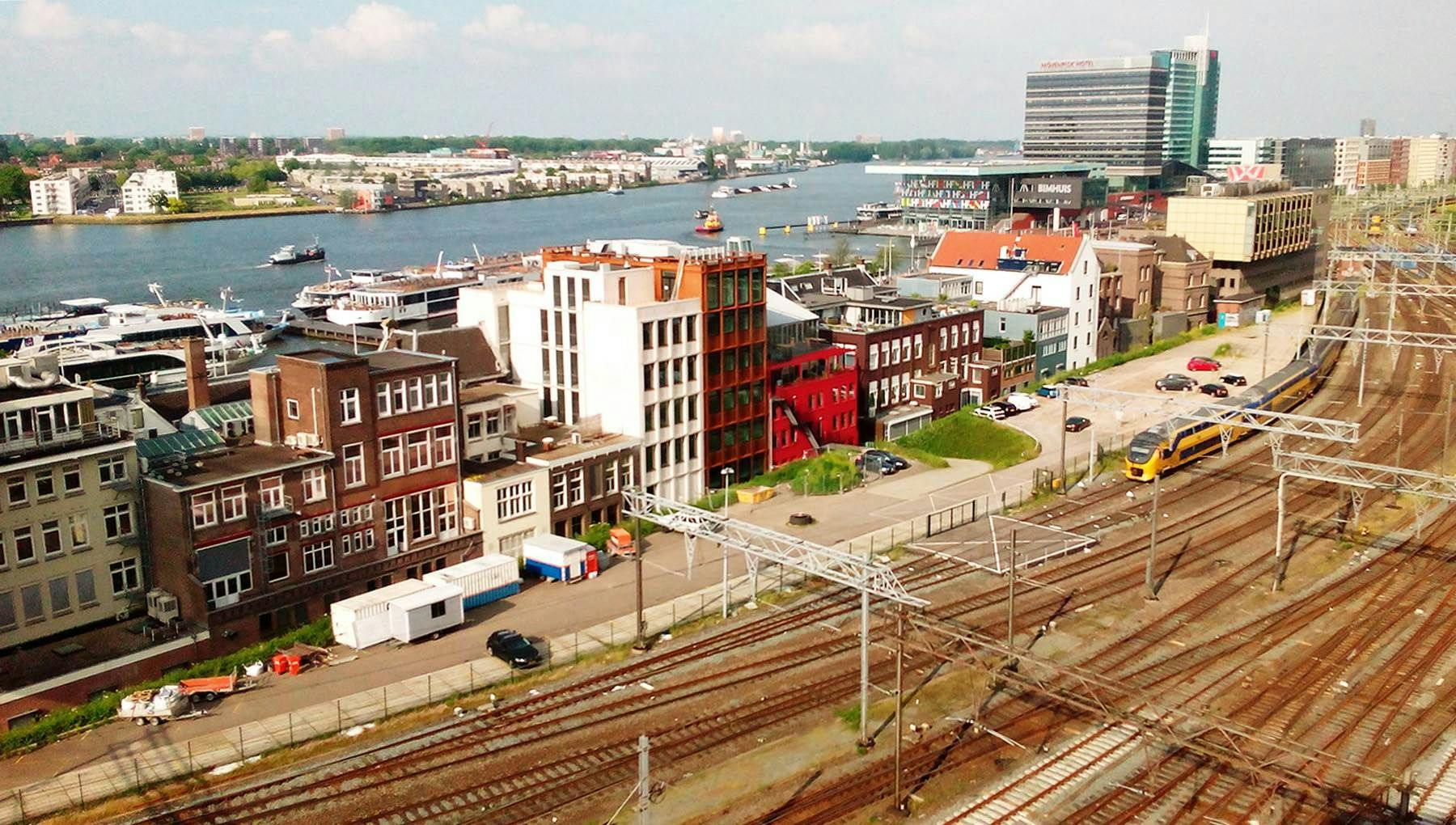 Train tracks in Amsterdam with IJ river visible behind buildings.