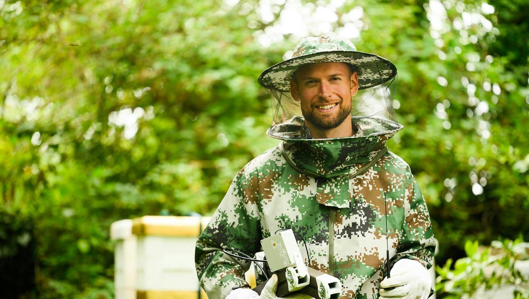 Cropped portrait of BeeSage founder Ru Wikmann wearing beekeeping outfit in pixelated camo colours.