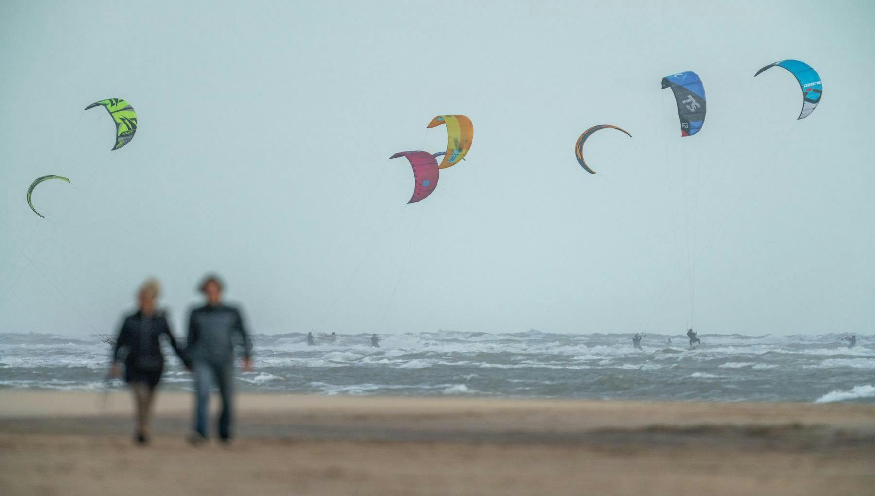 Couple walking over Amsterdam beach / On background kite surfers in action