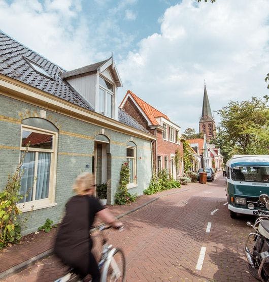 Woman cycling on Nieuwendammerdijk past Blue House traditional houses