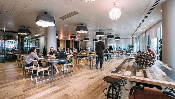 Long shot of people sat at tables in WeWork coworking space.