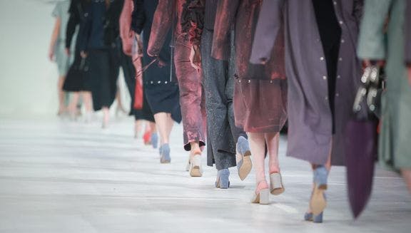 Models wearing violet and purple clothing on the catwalk during a fashion show.