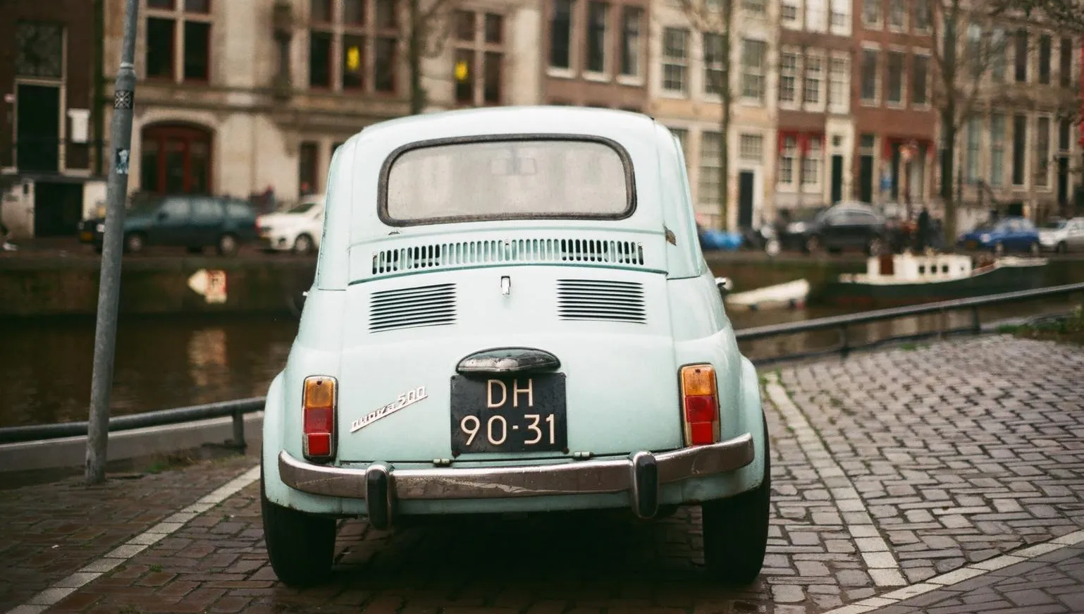 Blue vintage Fiat car parked by the canal.