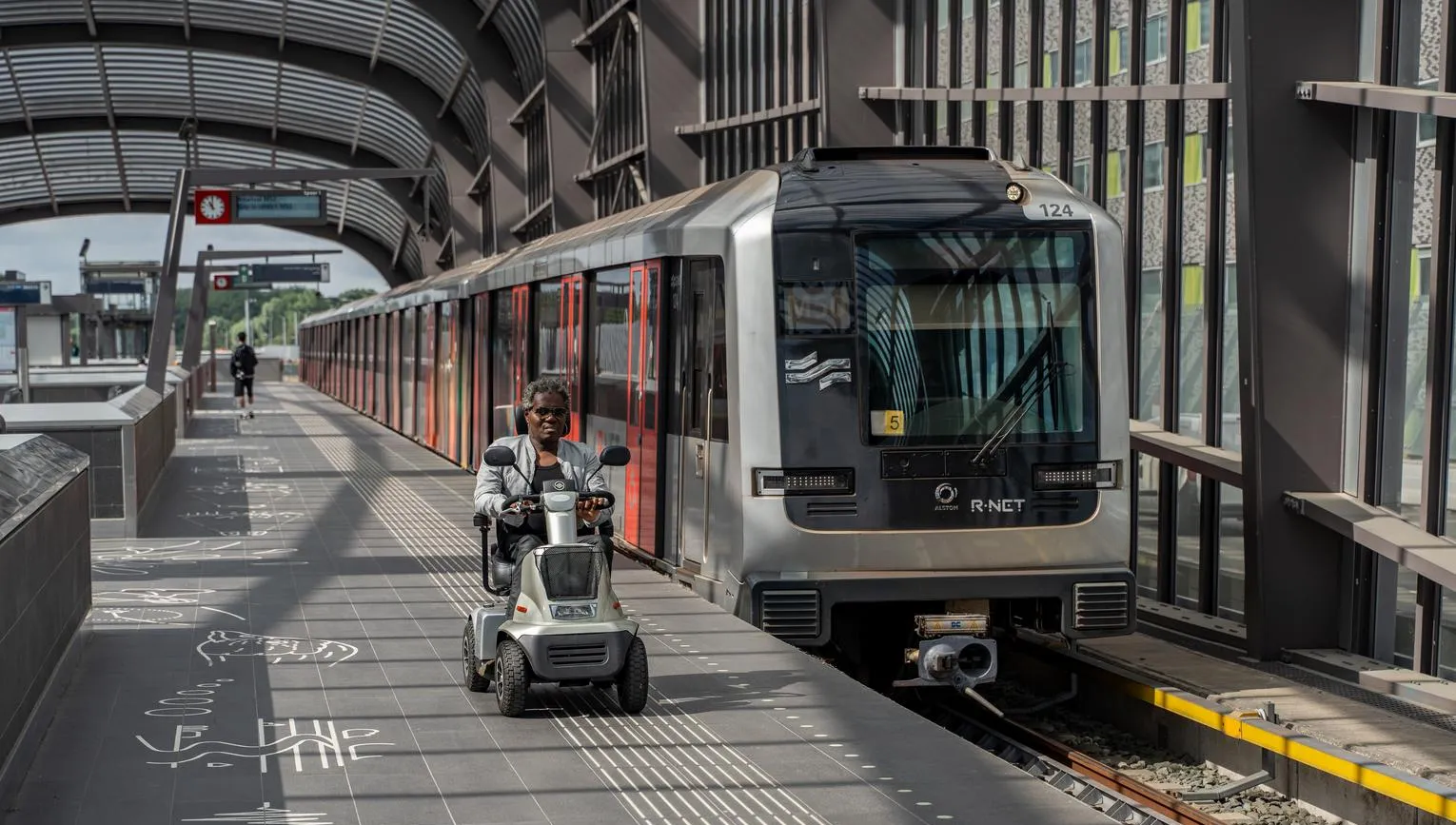 A person in an electric wheelchair riding on the metro platform.