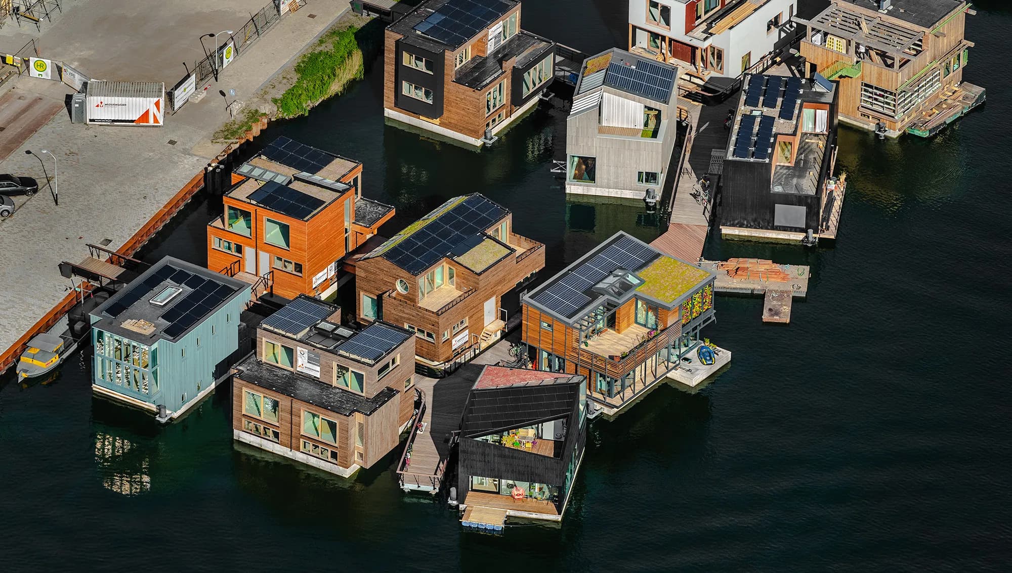 De dertien waterwoningen zijn door zes verschillende ontwerp partijen ontworpen, wat een divers aanzicht geeft. Allemaal hebben ze een betonnen drijflichaam en een opbouw van houtskeletbouw. Er zijn circa 500 zonnepanelen geïnstalleerd op de daken en douchen en afwassen gebeurt als het kan met opgevangen regenwater in een spaardouche. Het particulier opdrachtgeverschap Schoonschip bouwde samen met Bouwbedrijf van Middendorp deze drijvende wijk die in 2019 is opgeleverd. Foto John Gundlach.