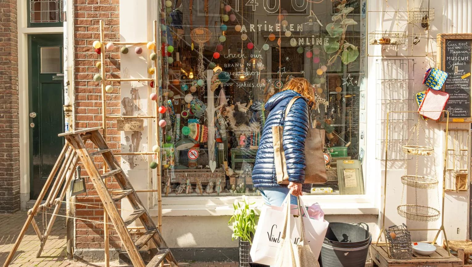 Woman with shopping bags looking in the window of Sjakies gift and concept store on shopping street. Haarlem Content Creation Day March 2024