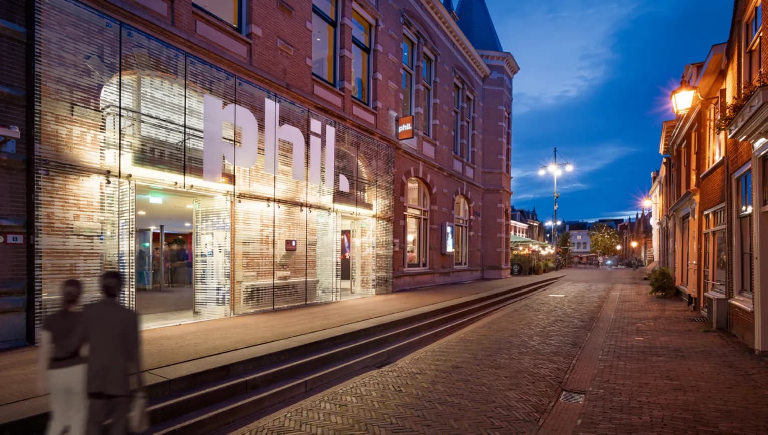 Couple walking past the exterior of PHIL Haarlem concert hall at night