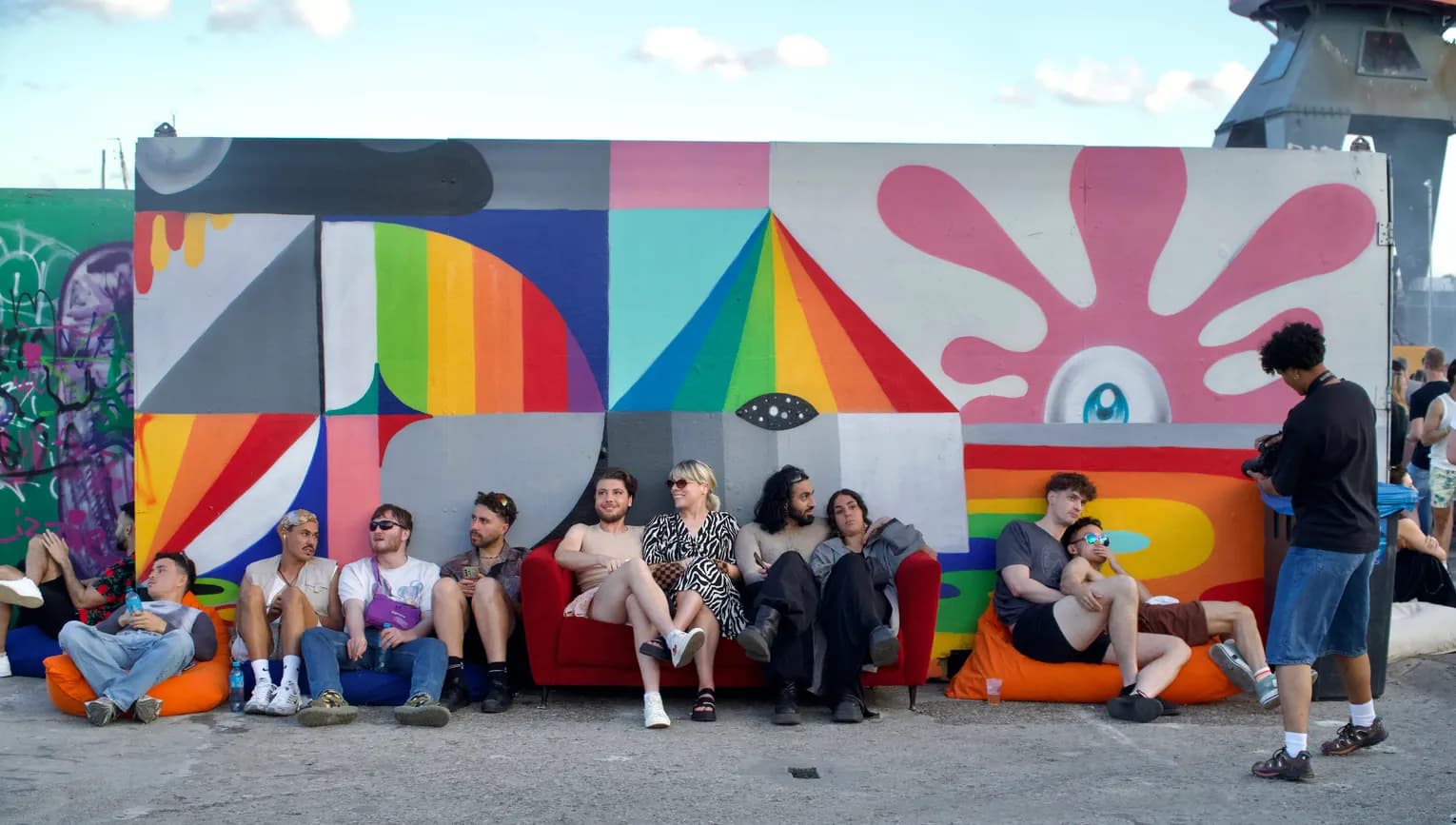 People lounging next a colourful wall at Tropikali Festival 2024.