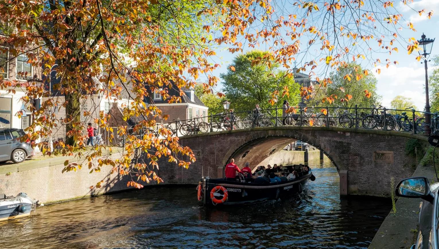 A tour boat passing by under the bridge on a sunny autumn day on Reguliersgracht.