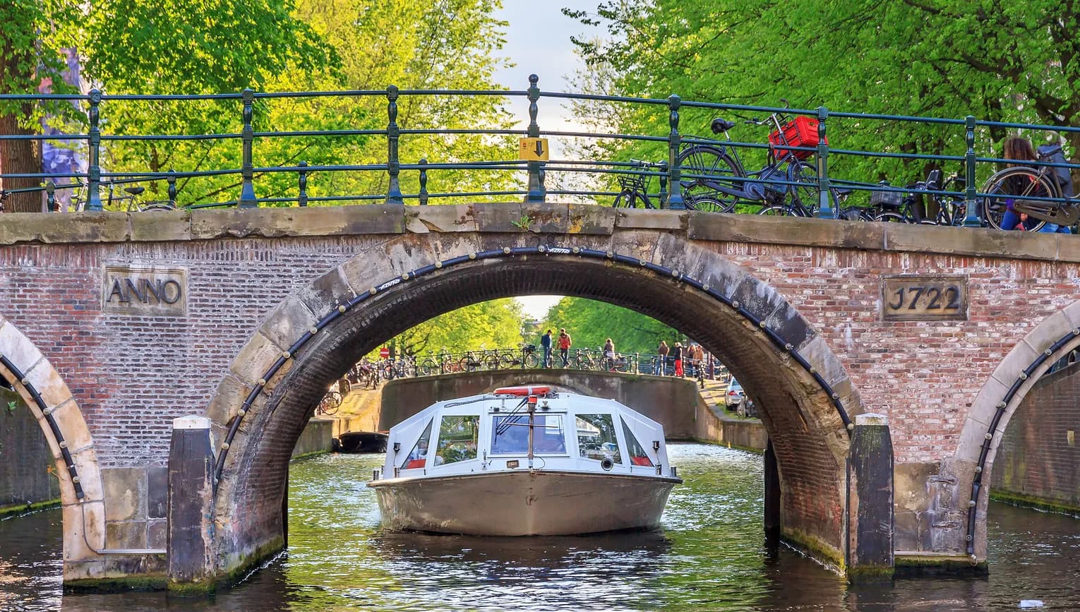 Canal cruise boat goes under the bridge over the Herengracht canal.