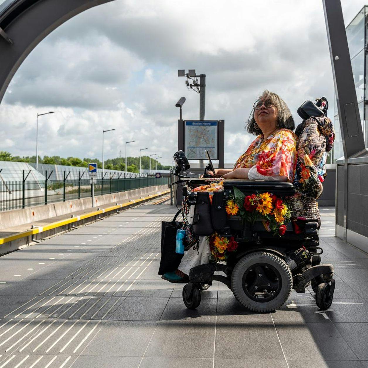 A person in an electric wheelchair on the platform waiting for the metro.