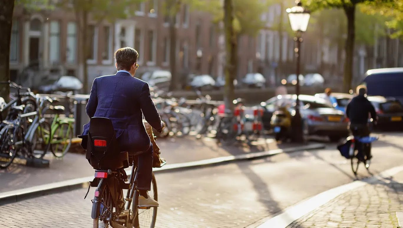 An elegantly dressed man rides a Bicycle in the center of Amsterdam. Bicycle capital of Europe.