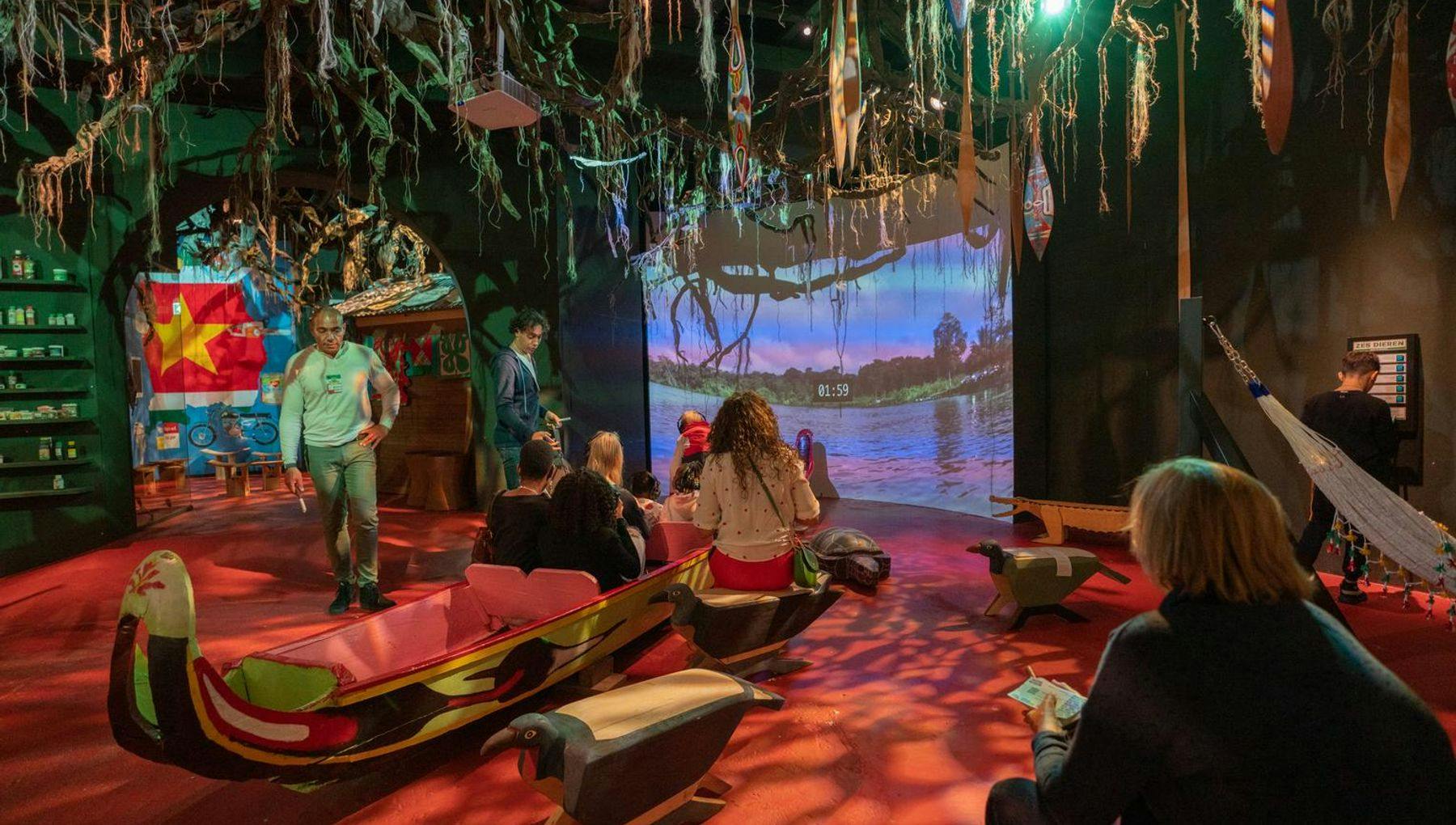 Visitors sitting in an indoor boat watching a screen at Sabi Suriname in Het Tropenmuseum during 24h Oost 2019