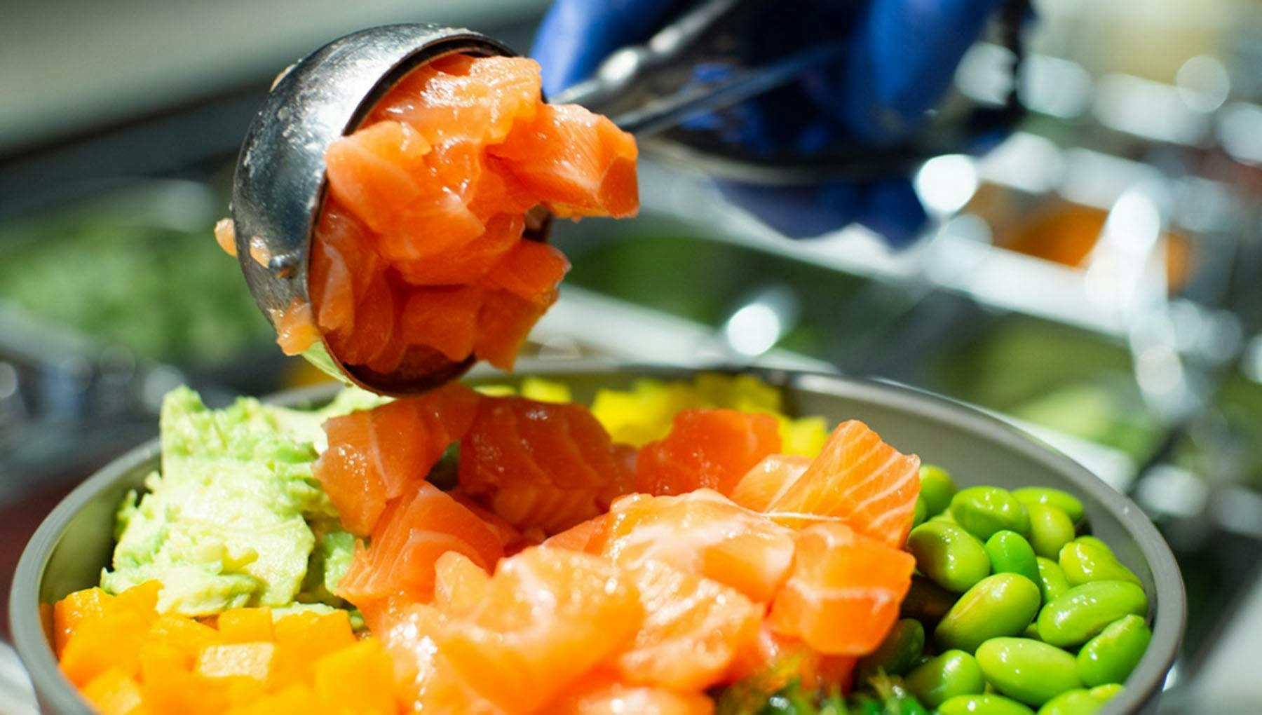 A gloved hand scooping pieces of salmon onto some vegetables.