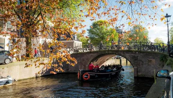 A tour boat passing by under the bridge on a sunny autumn day on Reguliersgracht.