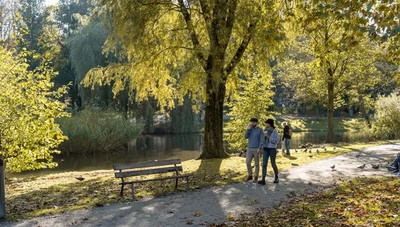A couple is walking through the Sarphatipark on a sunny autumn day.