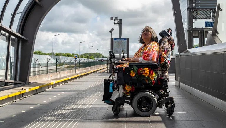 A person in an electric wheelchair on the platform waiting for the metro.