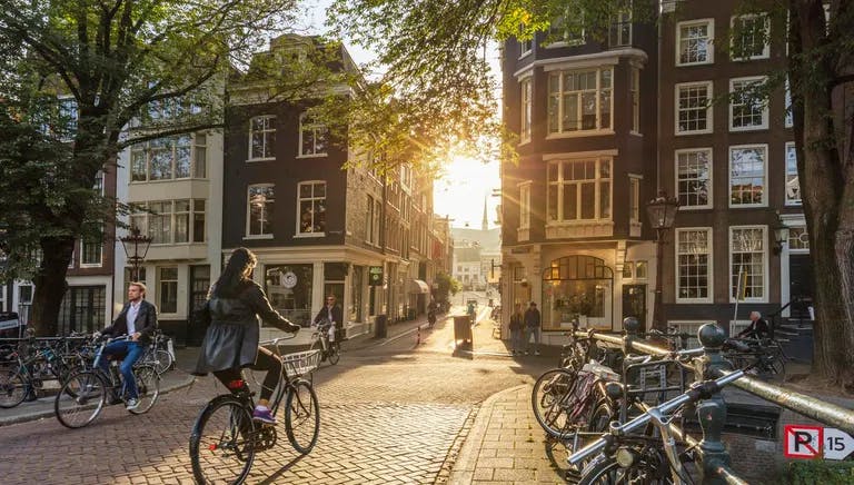 Amsterdam, Netherlands - September 22, 2021: Early morning in Amsterdam. Artistic image.  People ride bicycles, the ancient European city of Amsterdam. Sunlight and silhouettes, beautiful downtown houses.  Amsterdam, Holland, Netherlands, Europe