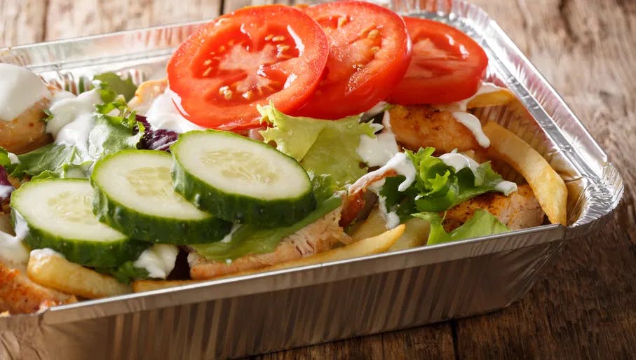 Delicious dinner Dutch kapsalon of french fries, chicken, fresh salad, cheese and sauce close-up in a foil tray on the table. horizontal