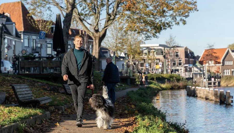 Man walks his dog over the walking path (parallel to Hoogstraat of Weesp) along the banks of Vecht river.