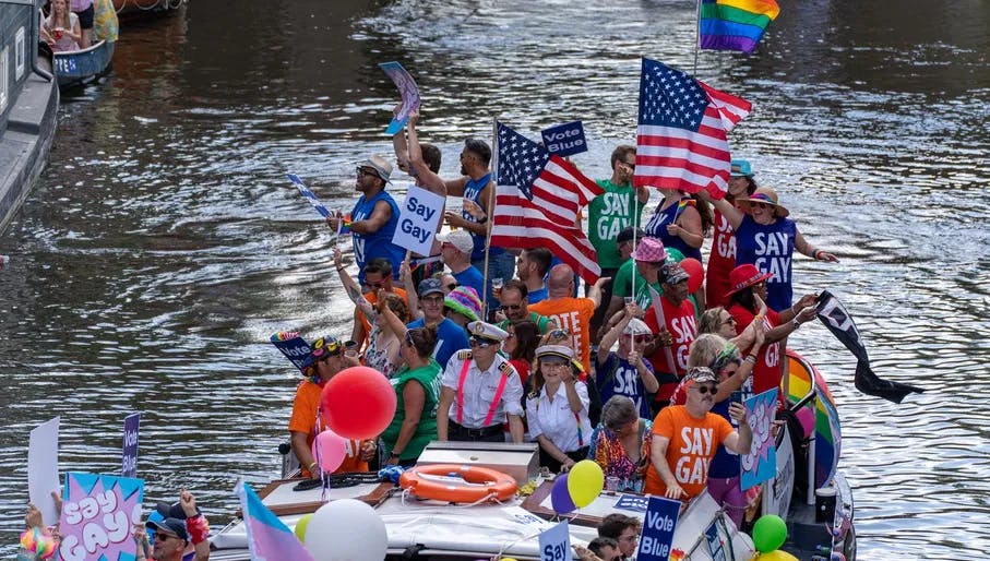 A group of people in a boat with flags and signs - Pride Canal Parade
