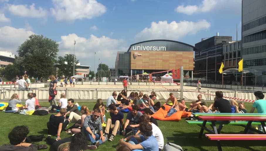 Students sitting on the grass in summer in front of University building of Physics UvA