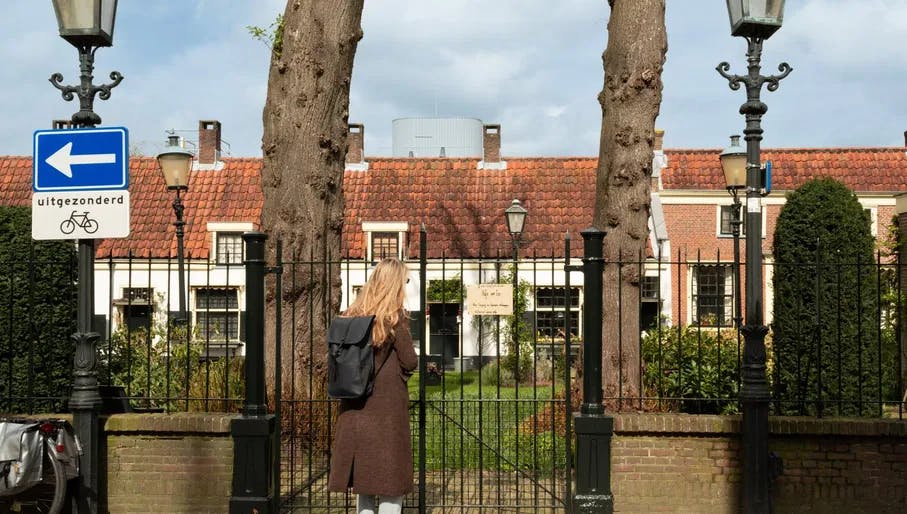 Woman with backpack peering into Hofje van Loo garden. Haarlem Content Creation Day March 2024