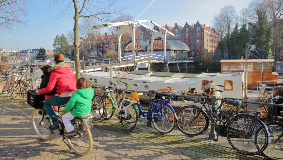 Family with two children cyling over the Sloterdijkerbrug bridge with bicycles and houseboats in the foreground, Prinseneiland, Amsterdam, Netherlands