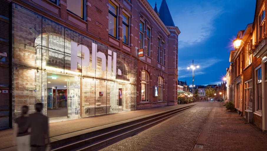 Couple walking past the exterior of PHIL Haarlem concert hall at night