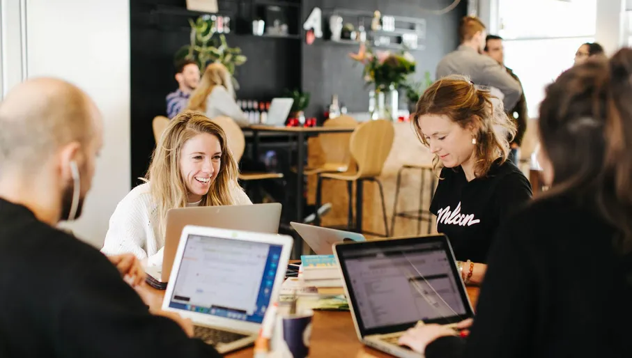 Four people at table with laptops in coworking space.